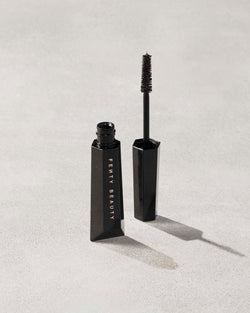 An open Fenty Hella Thicc mascara tube on a grey background. An open Fenty Hella Thicc mascara tube on a grey background.