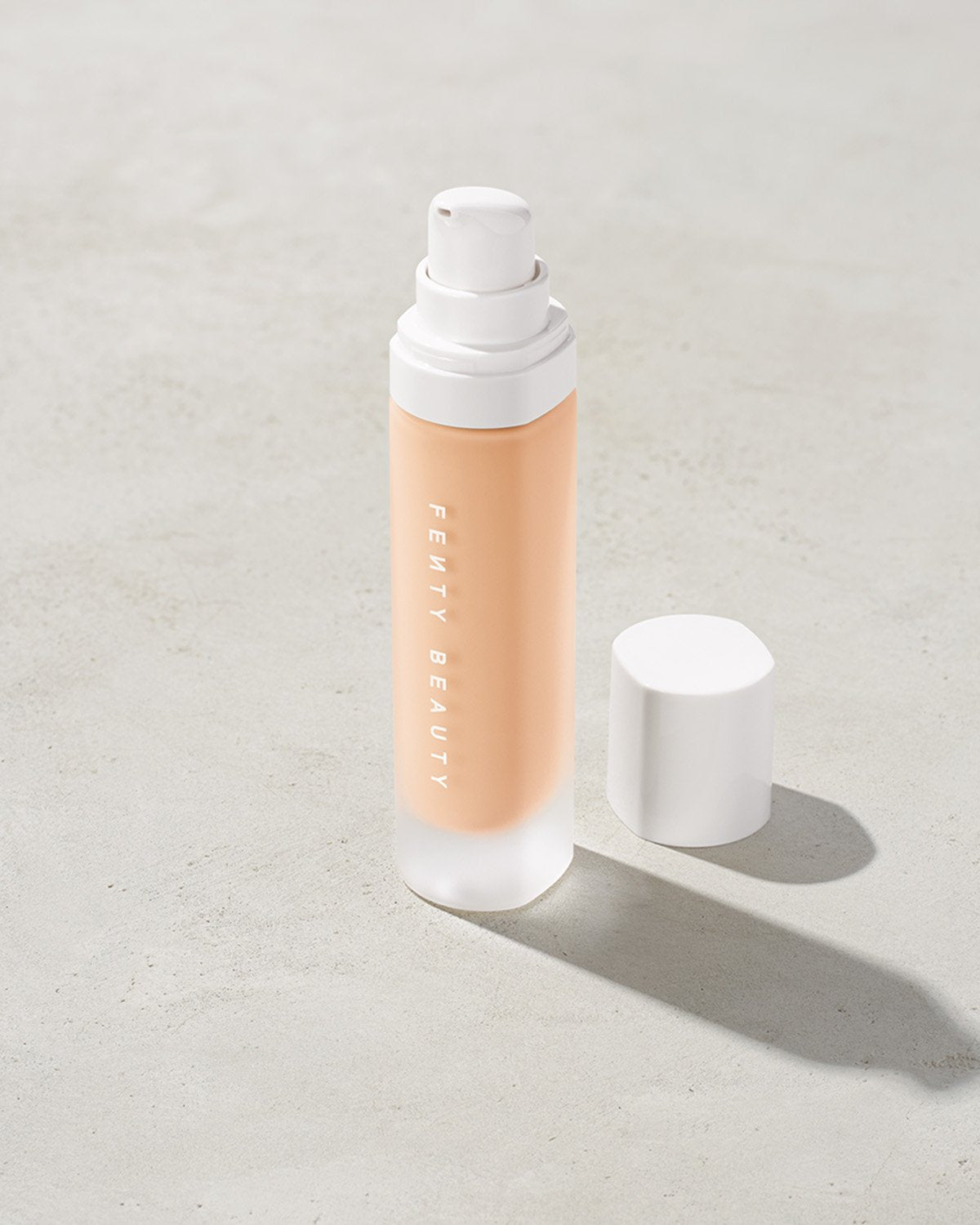 open bottle of Fenty Beauty Pro Filt'r Soft Matte Longwear Foundation with pump dispenser in shade #100 on concrete background