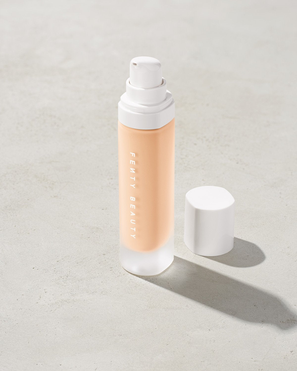 open bottle of Fenty Beauty Pro Filt'r Soft Matte Longwear Foundation with pump dispenser in shade #110 on concrete background