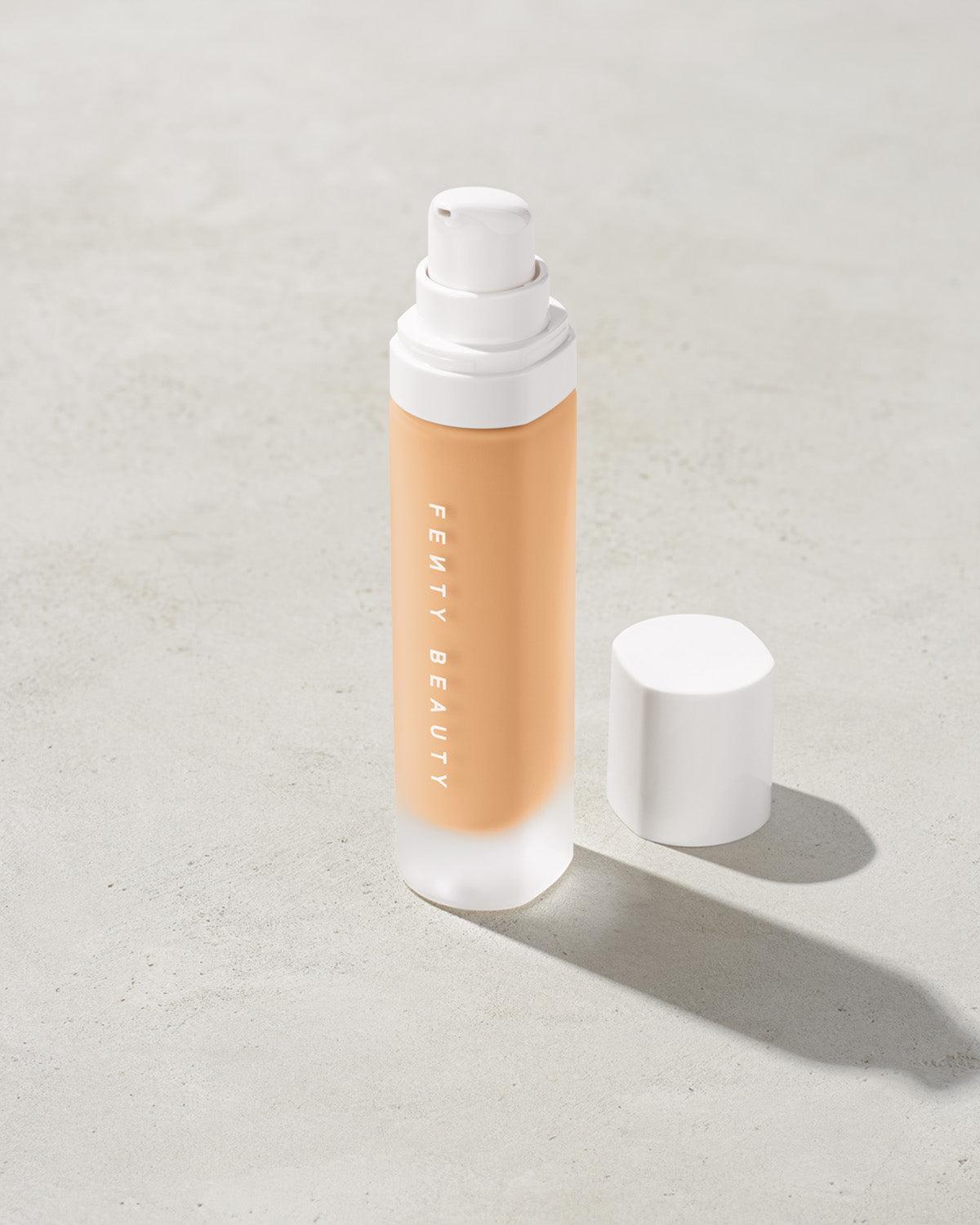 open bottle of Fenty Beauty Pro Filt'r Soft Matte Longwear Foundation with pump dispenser in shade #200 on concrete background