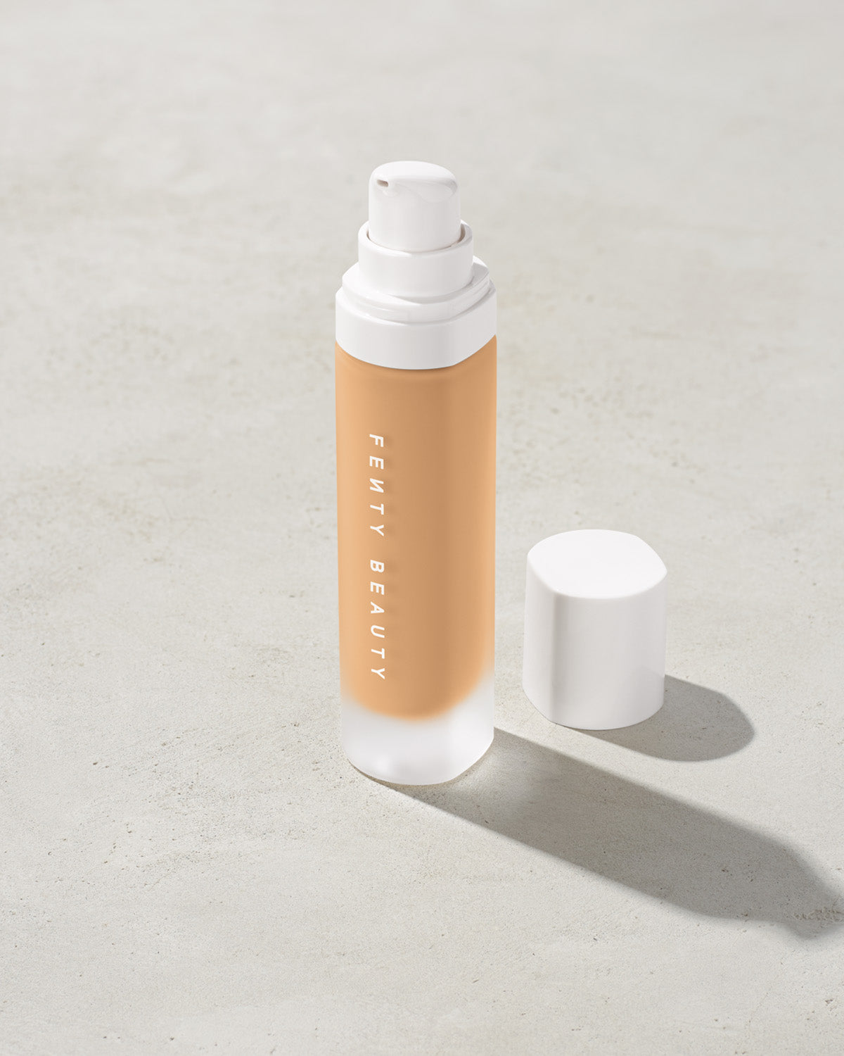 open bottle of Fenty Beauty Pro Filt'r Soft Matte Longwear Foundation with pump dispenser in shade #240 on concrete background