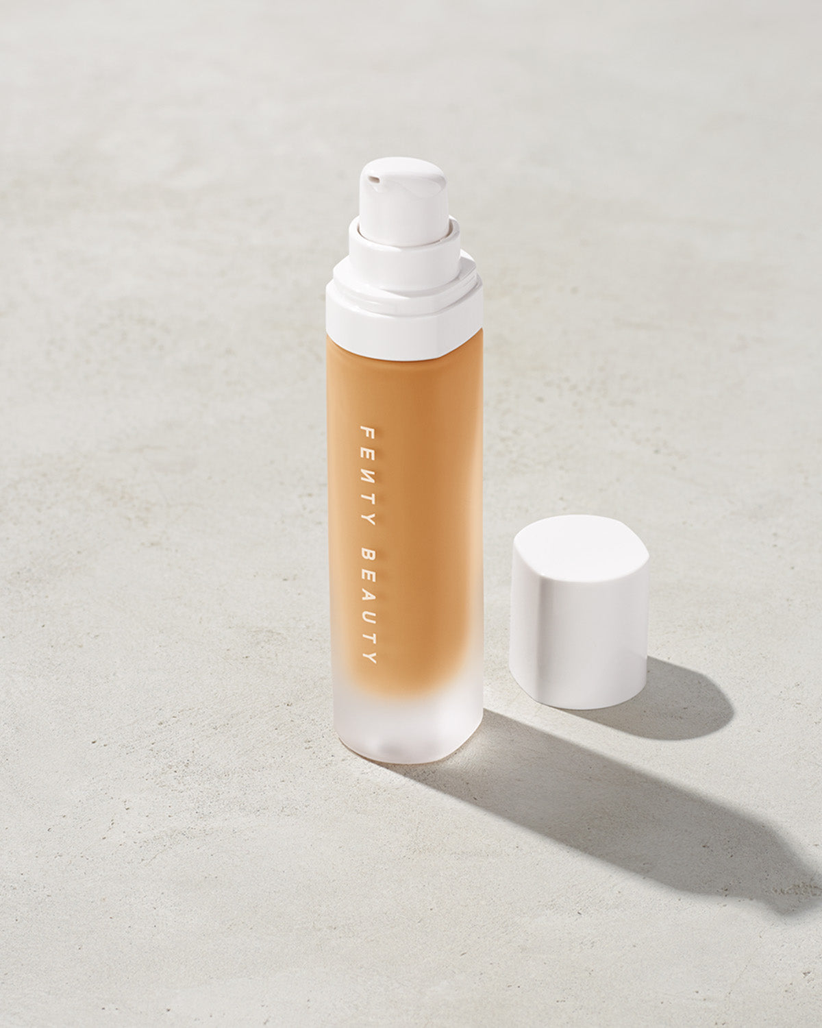 open bottle of Fenty Beauty Pro Filt'r Soft Matte Longwear Foundation with pump dispenser in shade 300 on concrete background