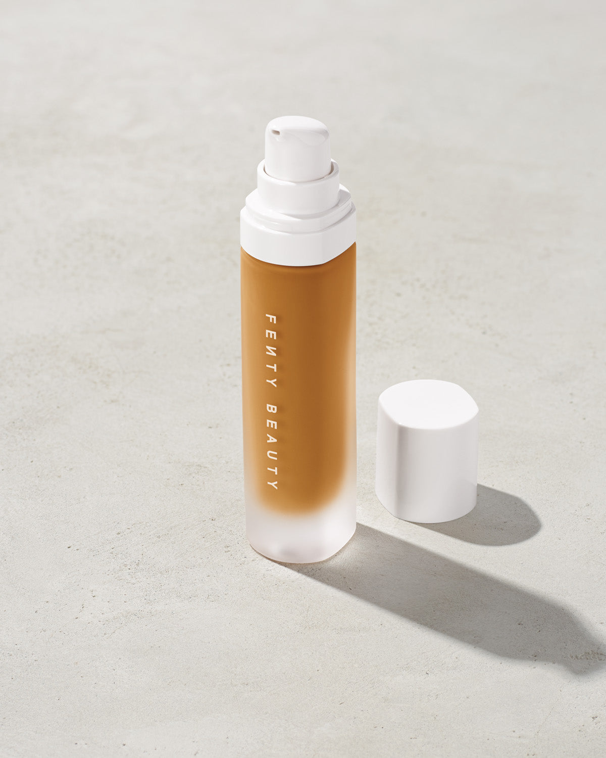 open bottle of Fenty Beauty Pro Filt'r Soft Matte Longwear Foundation with pump dispenser in shade 350 on concrete background