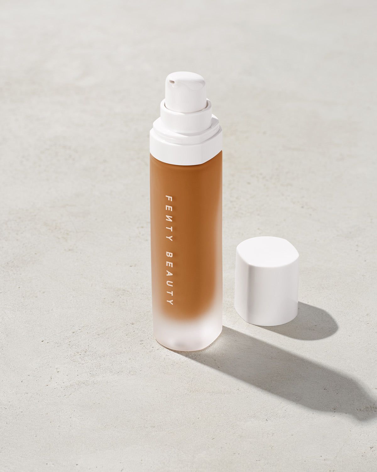 open bottle of Fenty Beauty Pro Filt'r Soft Matte Longwear Foundation with pump dispenser in shade 410 on concrete background