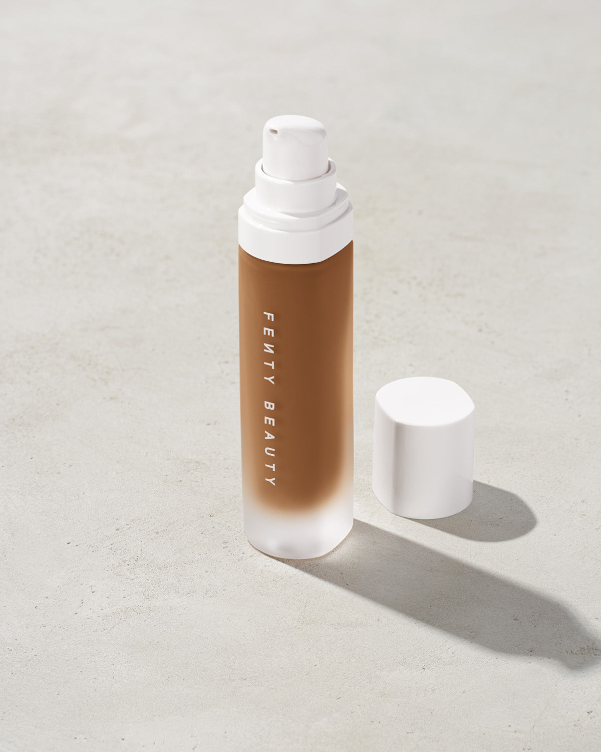 open bottle of Fenty Beauty Pro Filt'r Soft Matte Longwear Foundation with pump dispenser in shade 450 on concrete background