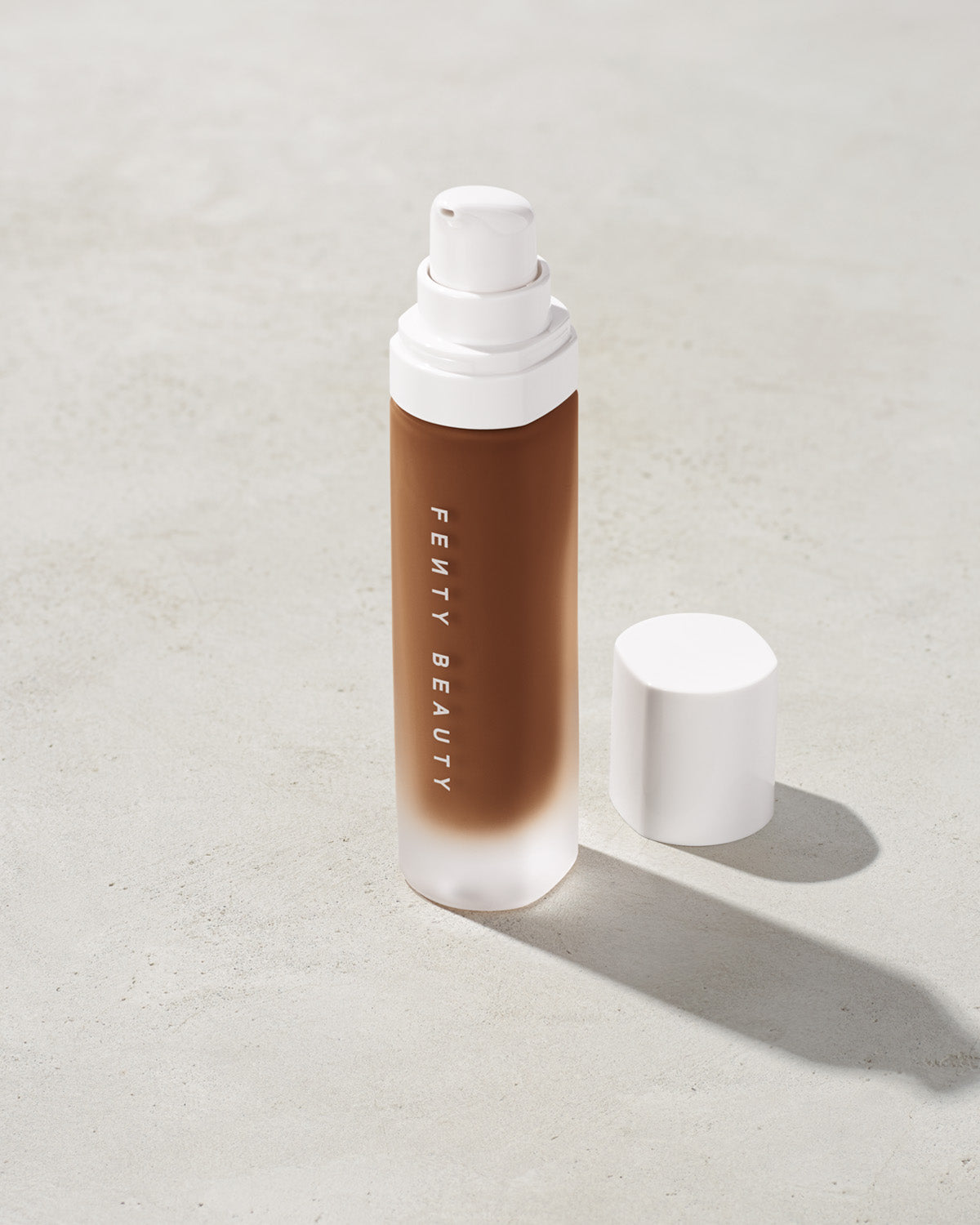 open bottle of Fenty Beauty Pro Filt'r Soft Matte Longwear Foundation with pump dispenser in shade 480 on concrete background