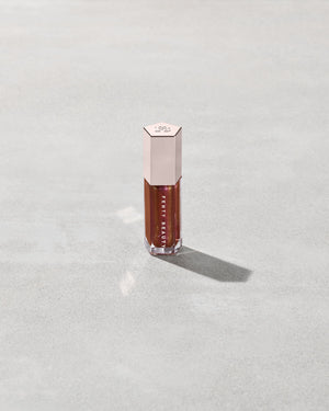 A close tube of Gloss Bomb Universal Lip Luminizer in the shade Hot Chocolit Fantasy on a grey background.