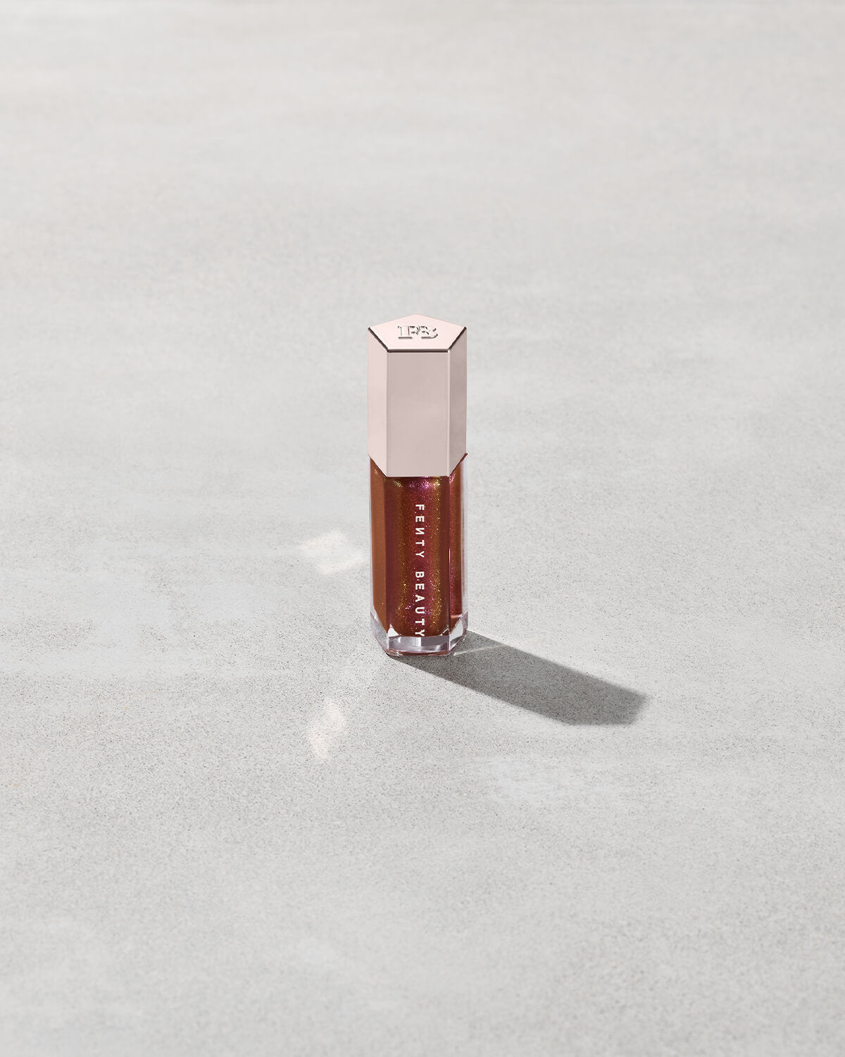 A close tube of Gloss Bomb Universal Lip Luminizer in the shade Hot Chocolit Fantasy on a grey background.