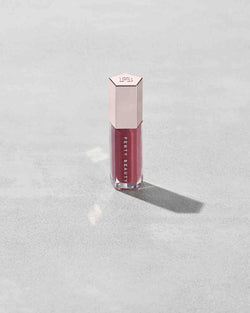A closed tube of Gloss Bomb Universal Lip Luminizer in the shade RiRi on a grey background. A closed tube of Gloss Bomb Universal Lip Luminizer in the shade RiRi on a grey background.