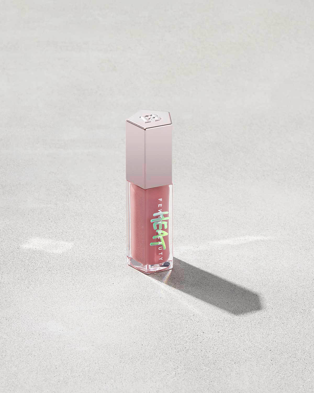 tube of Fenty Beauty Gloss Bomb Heat Universal Lip Luminizer + Plumper in shade Fussy Heat on concrete background