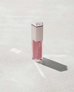 A closed tube of Gloss Bomb Universal Lip Luminizer in the shade Fu$$y on a grey background. A closed tube of Gloss Bomb Universal Lip Luminizer in the shade Fu$$y on a grey background.