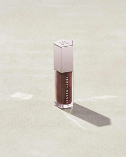 A closed tube of Gloss Bomb Universal Lip Luminizer in the shade Hot Chocolit on a grey background. A closed tube of Gloss Bomb Universal Lip Luminizer in the shade Hot Chocolit on a grey background.