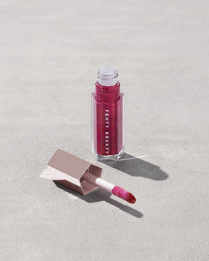 An open tube of Gloss Bomb Universal Lip Luminizer in the shade Fuchsia Flex on a grey background.