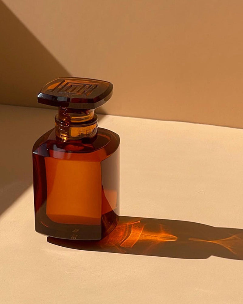 Fenty Eau de Parfum clear chestnut brown tinted glass perfume bottle on a peachy tan surface