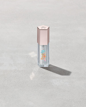 Closed tube of Gloss Bomb Heat lip gloss and plumper in the shade Glass Slipper on a grey background.