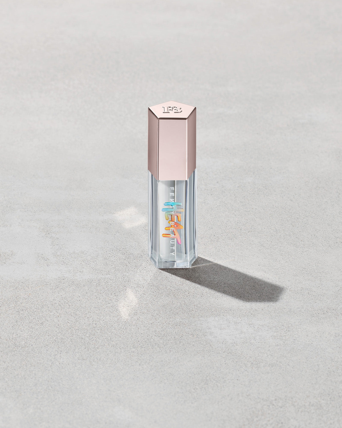 Closed tube of Gloss Bomb Heat lip gloss and plumper in the shade Glass Slipper on a grey background.