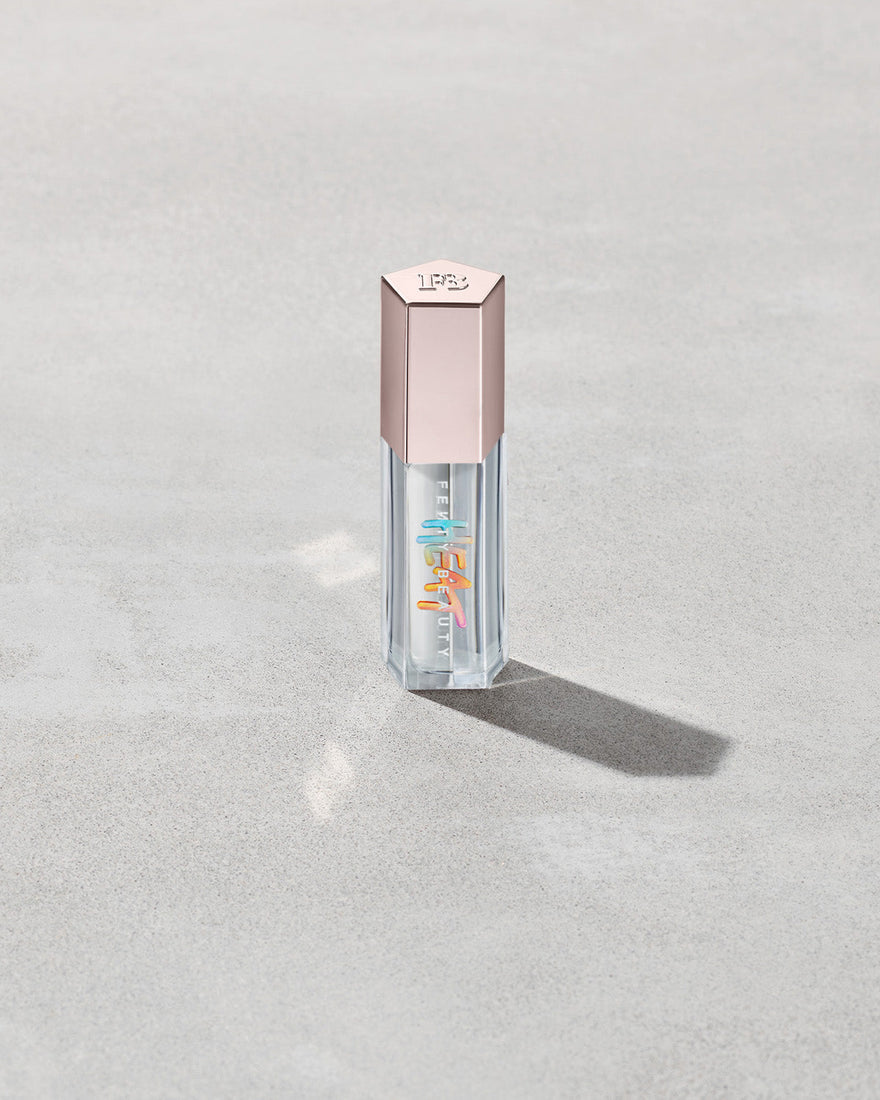 Closed tube of Gloss Bomb Heat lip gloss and plumper in the shade Glass Slipper on a grey background.