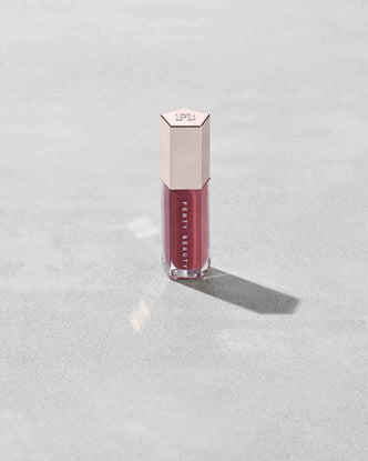 A closed tube of Gloss Bomb Universal Lip Luminizer in the shade RiRi on a grey background.