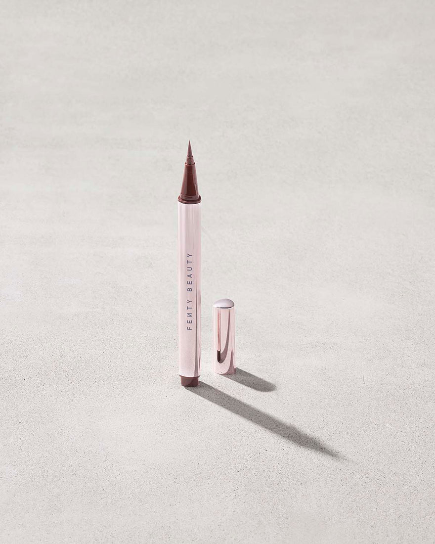 Fenty Beauty Flyliner Longwear Liquid Eyeliner in shade In Big Truffle with cap off on concrete background