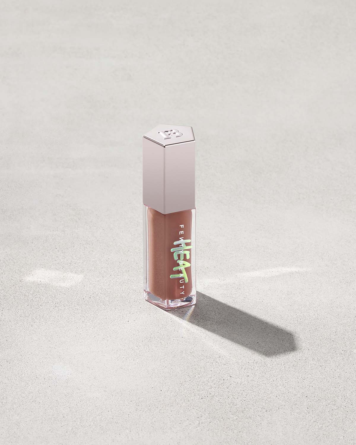tube of Fenty Beauty Gloss Bomb Heat Universal Lip Luminizer + Plumper in shade Fenty Glow Heat on concrete background