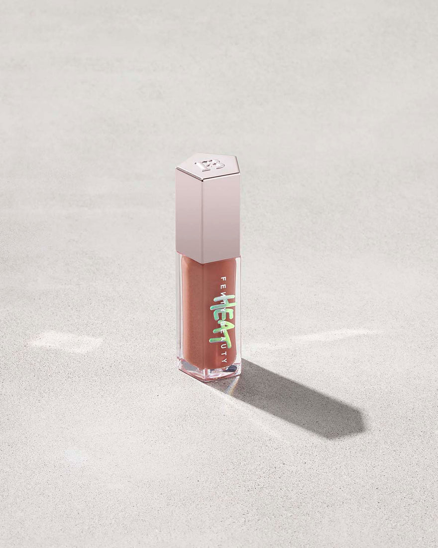 tube of Fenty Beauty Gloss Bomb Heat Universal Lip Luminizer + Plumper in shade Fenty Glow Heat on concrete background