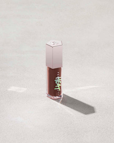 tube of Fenty Beauty Gloss Bomb Heat Universal Lip Luminizer + Plumper in shade Hot Chocolit Heat on concrete background