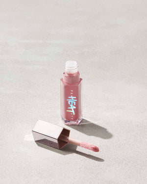 open tube of Fenty Beauty Gloss Bomb Heat Universal Lip Luminizer + Plumper in shade Fussy Heat with doe foot applicator on concrete background