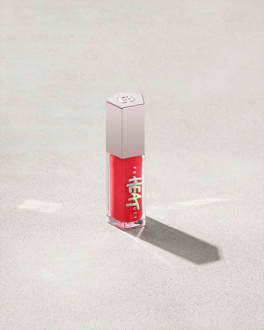 Closed tube of Gloss Bomb Heat lip gloss and plumper in the shade Hot Cherry on a grey background.